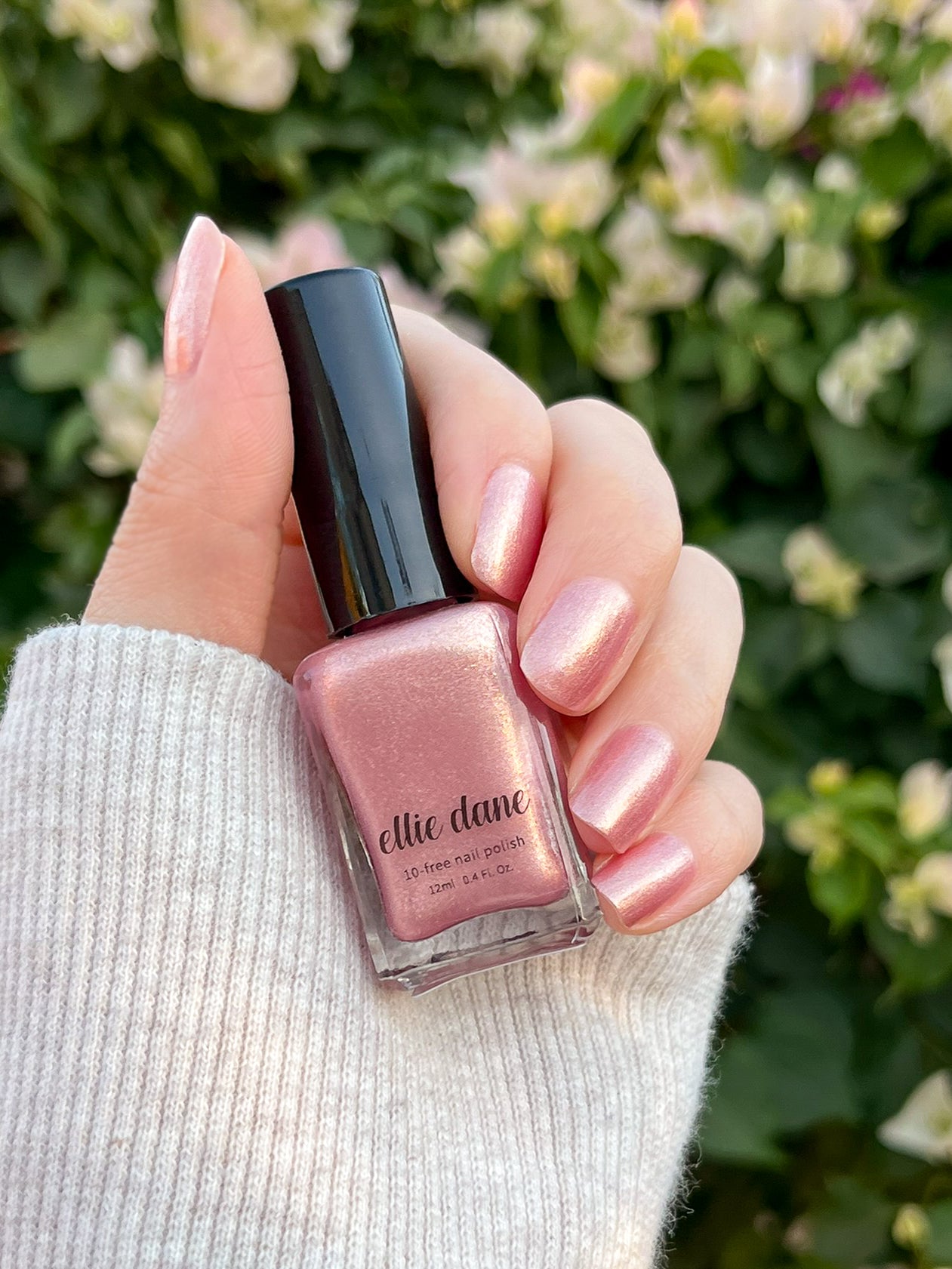 Champagne, Please painted on nails holding nail polish bottle with flowers in the background