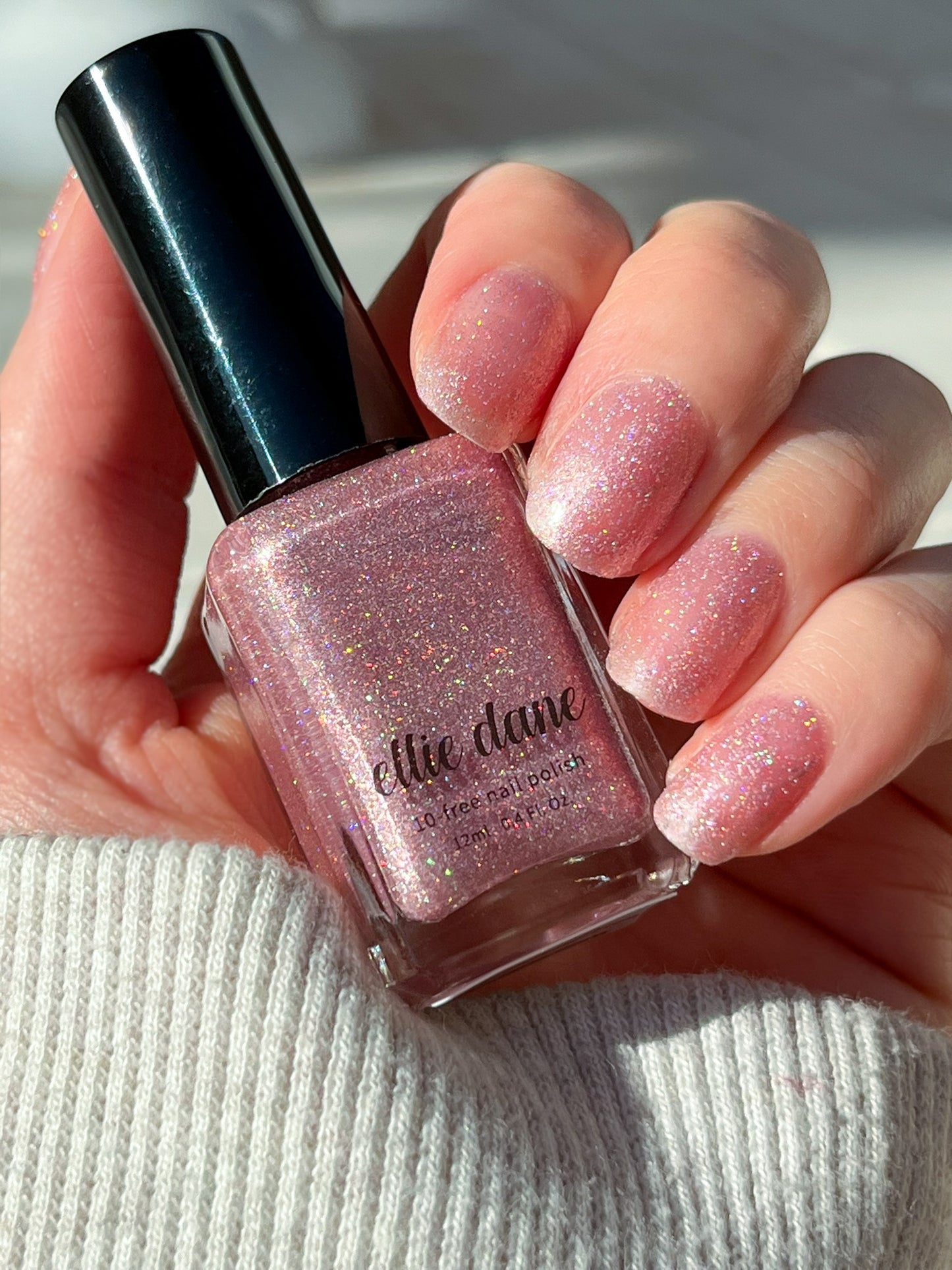 Hand swatch of Rose Quartz pink nail polish bottle in direct sunlight