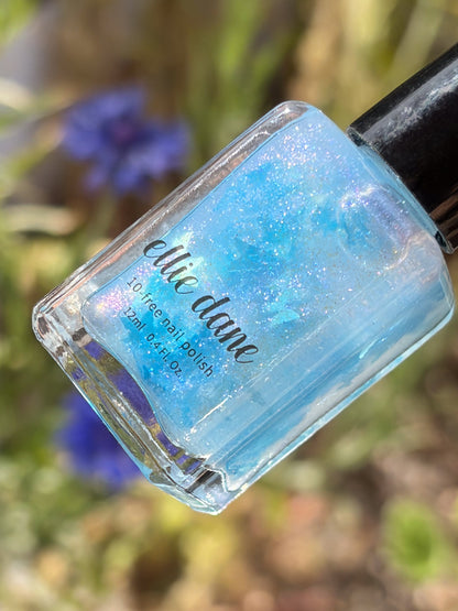 Blue glittery butterfly nail polish bottle with a blurred natural background