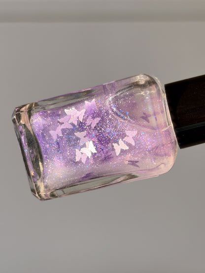 Nail polish bottle with purple glitter and butterfly design on a gray background